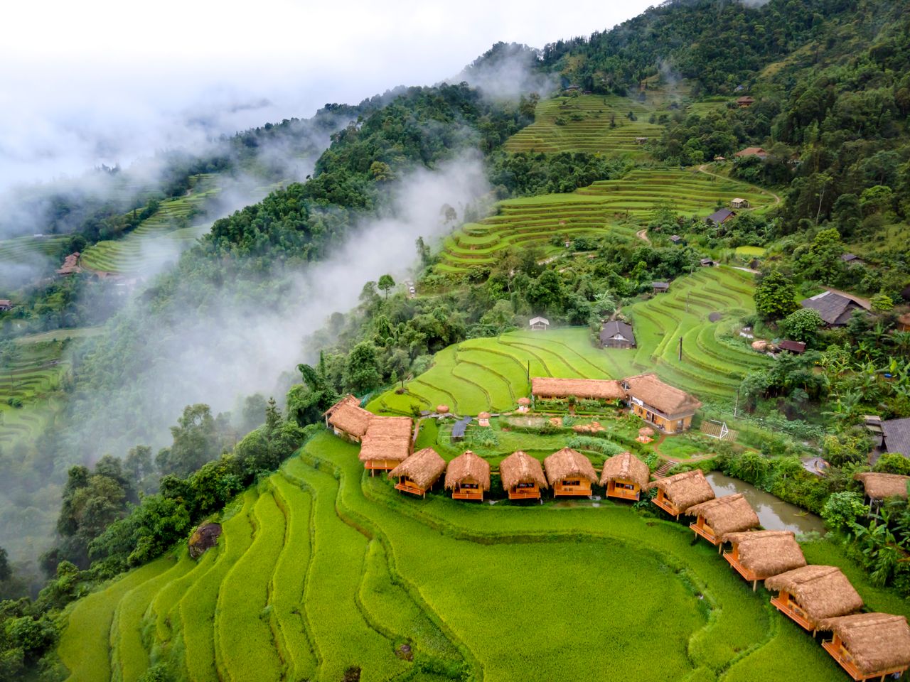 Breathtaking aerial shot of terraced rice fields and thatched huts surrounded by lush greenery and mist.